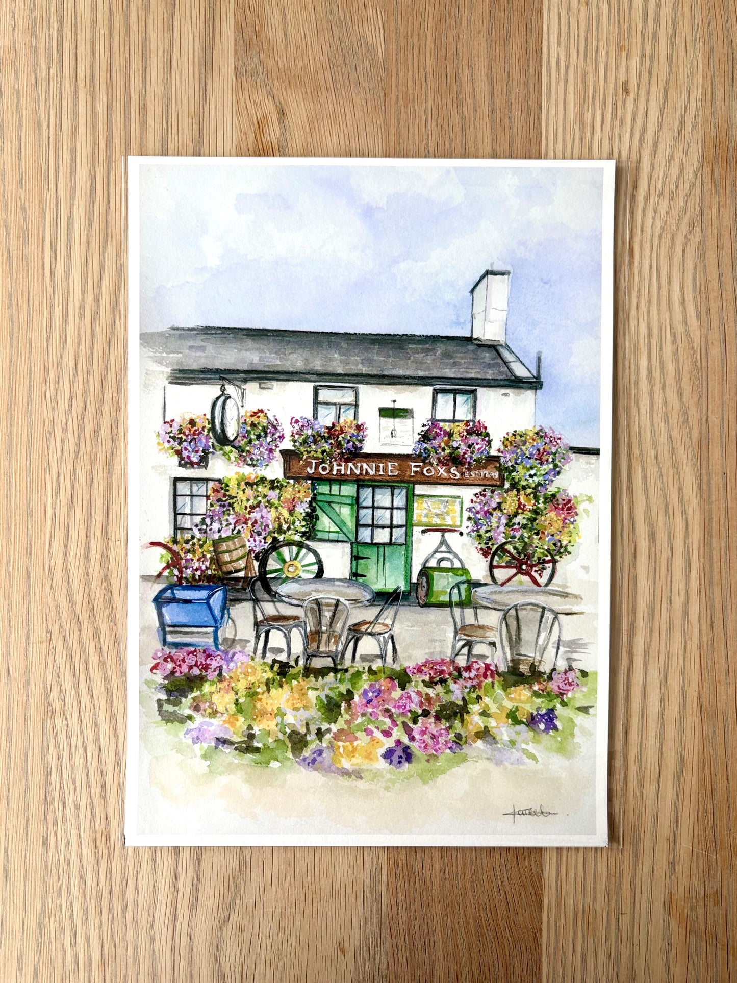 Watercolor painting of a quaint pub with floral decorations on a wooden surface