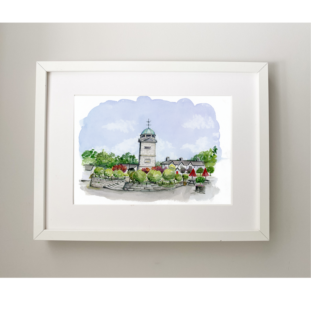 Framed artwork of a town scene with a clock tower on a light gray wall.