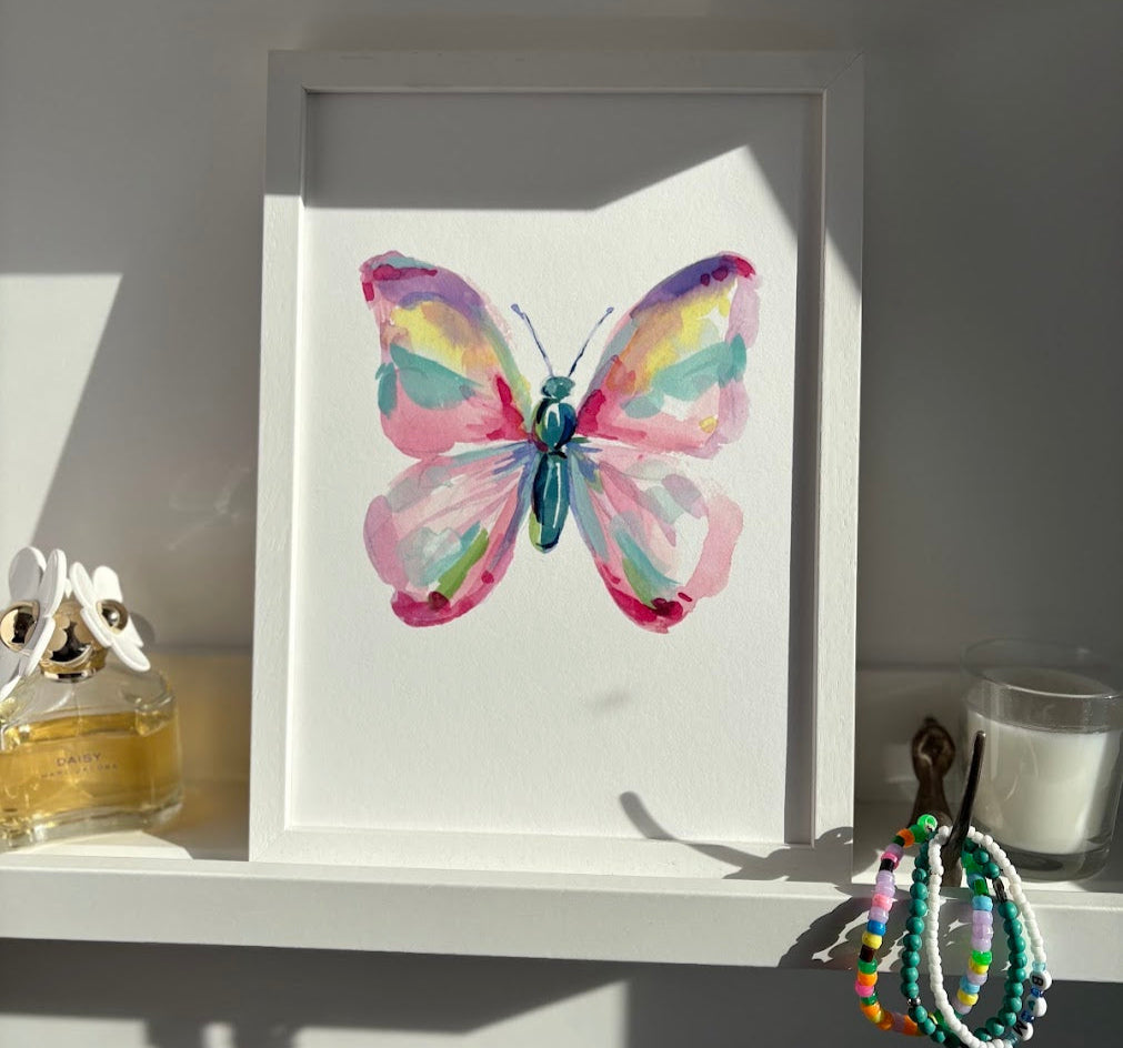 Framed watercolor butterfly artwork on a shelf with decorative items.