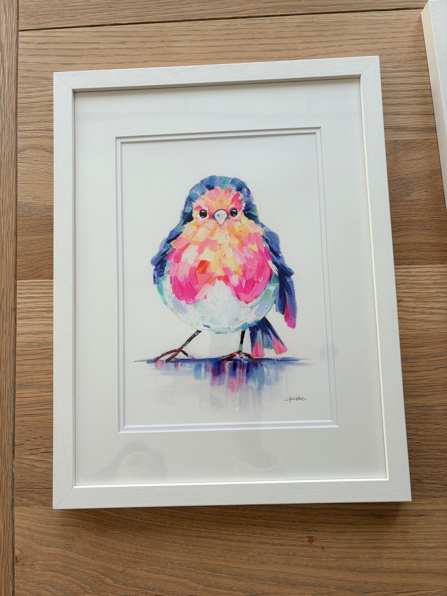 Framed watercolor painting of a colorful bird on a wooden surface