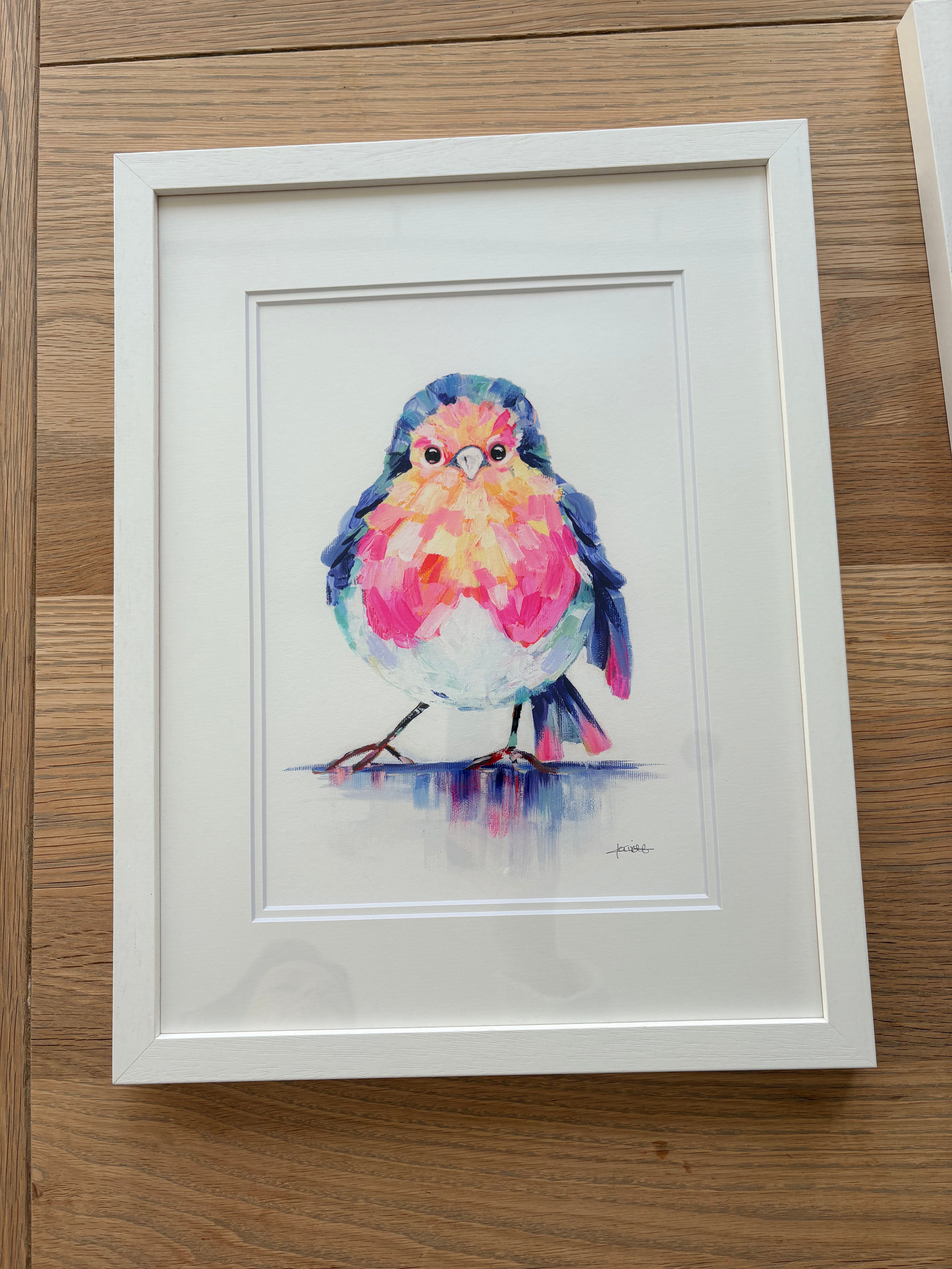 Framed watercolor painting of a colorful bird on a wooden surface